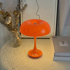 An orange mushroom-shaped LED table lamp with a slender stem sits on a white textured surface.