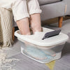 A white collapsible foot spa bucket containing a foot, used for massage or soaking.