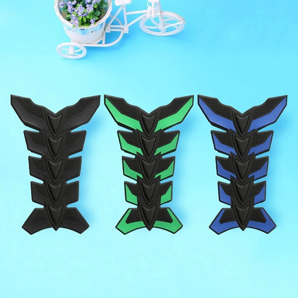 Three motorcycle tank pad protectors in black, green, and blue fish bone designs displayed on a light blue background.