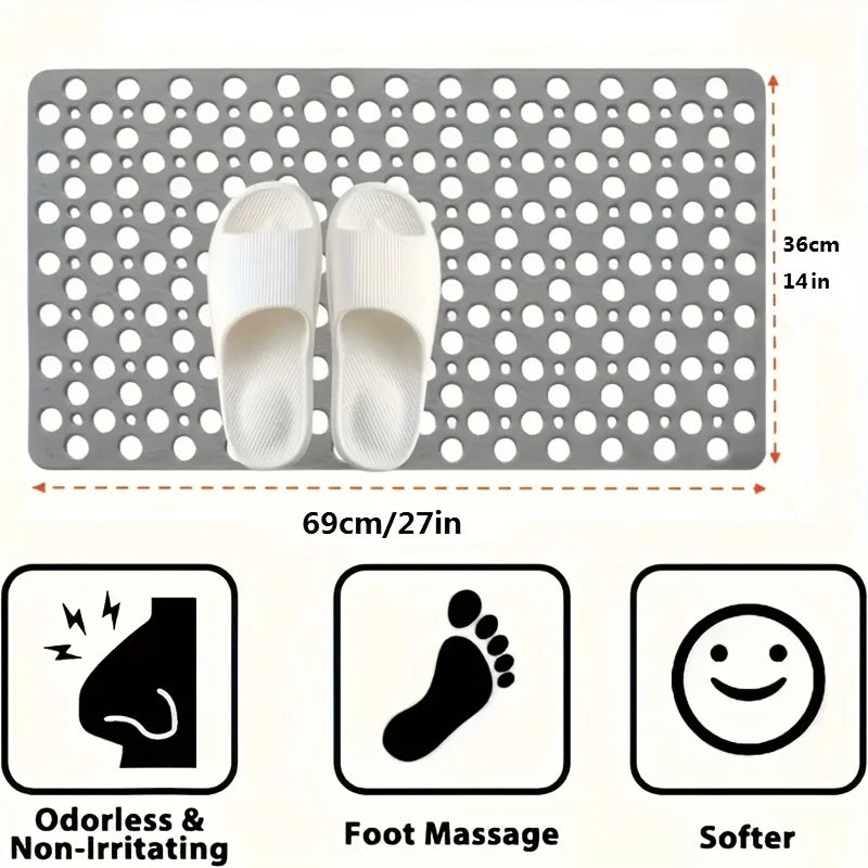A gray anti-slip shower mat with drainage holes and massage points, shown next to a pair of white flip-flops.