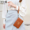 A woman holds a brown leather passport wallet with a strap against a light blue skirt.