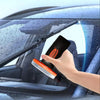 A hand is using a glass oil film remover cleaning brush to clean a car window.