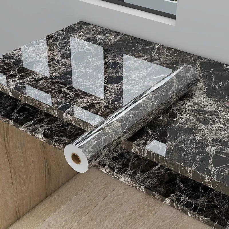 Roll of marble effect self-adhesive PVC film with a geometric pattern placed on a black marble countertop.