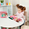 A young girl is engaging with a pink felt activity book and related materials on a white table.