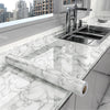 A modern kitchen countertop with a stainless steel sink and a marble peel-and-stick wallpaper roll visible.