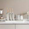 A white organizer rack holds several white spatulas with wooden handles on a marble countertop.