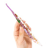A hand holds a clear epoxy resin floral-patterned crochet hook set with purple handles and embedded flowers.