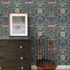 A dark wooden dresser with a framed picture and a wooden chair set against blue vintage damask floral wallpaper.