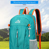 A teal foldable portable mountaineering backpack with orange accents shown outdoors on a grassy field.