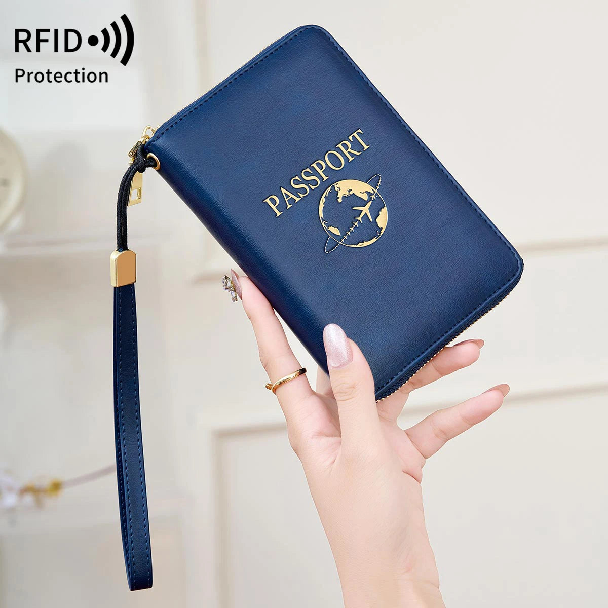 A hand holds a dark blue RFID blocking passport wallet with a gold emblem and a matching wrist strap.