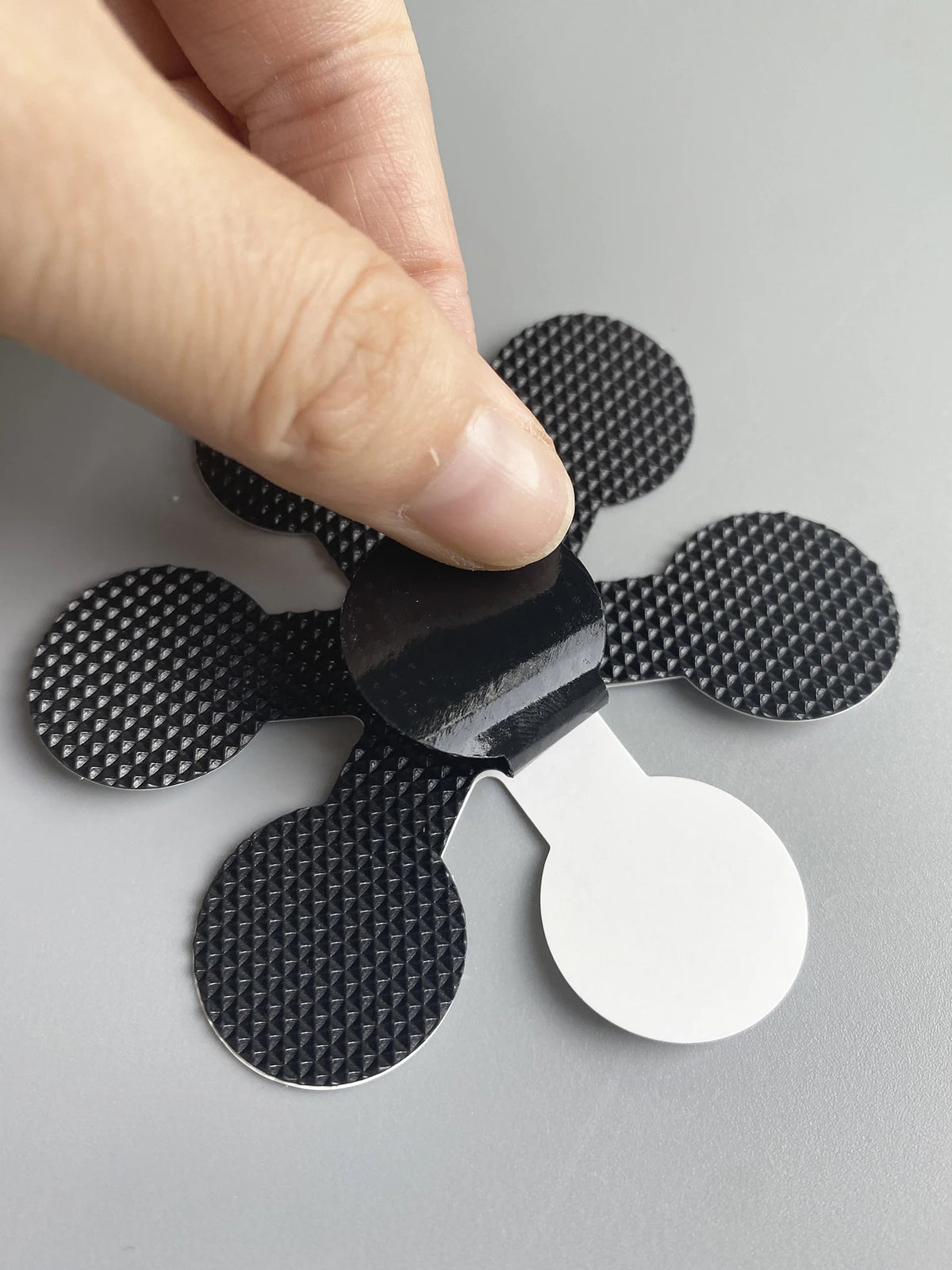 A hand is applying a black anti-slip shower sticker to a white surface.