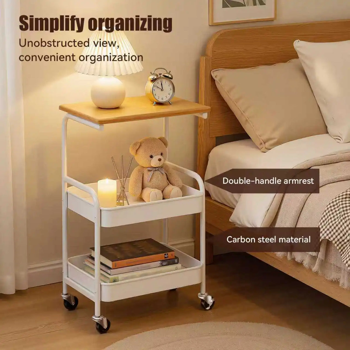 A white 3-tier rolling utility cart with a wooden top, holding a lamp and a teddy bear, next to a wooden bed frame.