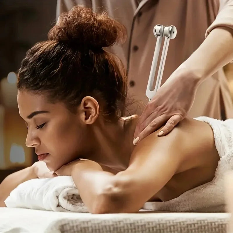 A woman is receiving sound therapy using a tuning fork set on her shoulder during a healing session.