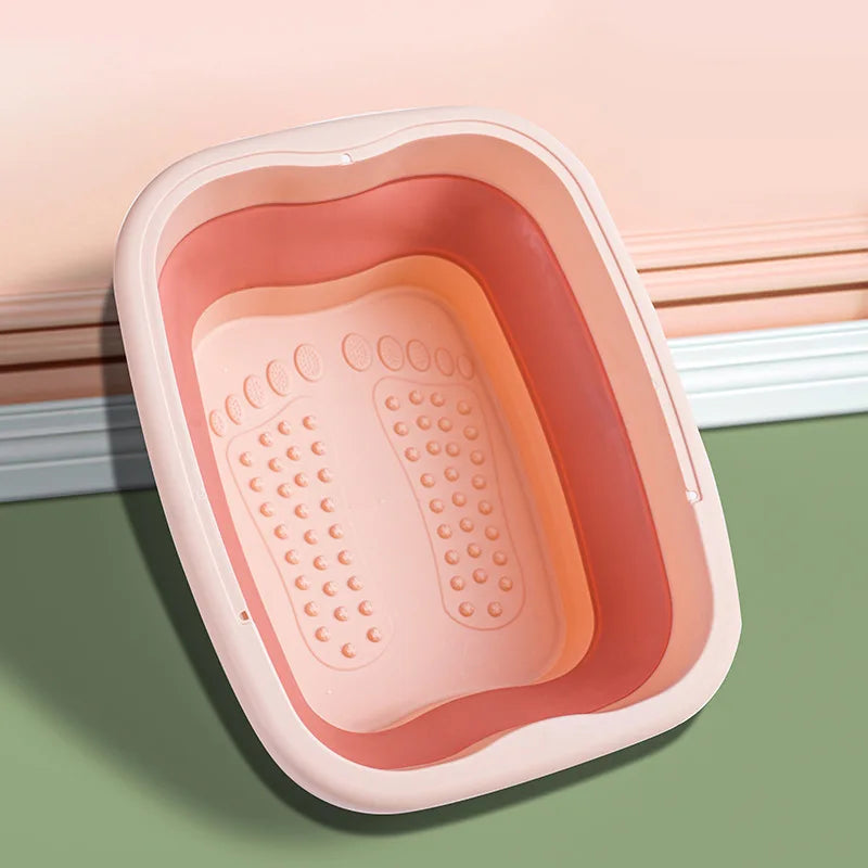 A pink collapsible foot spa bucket with massage nodules resting on a green surface.
