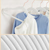 A white velvet hanger with a curved hook is shown hanging on a wooden rod, next to a blue sweater.
