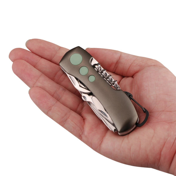 A hand holds a compact multi-tool keychain knife with a silver finish and three green buttons.