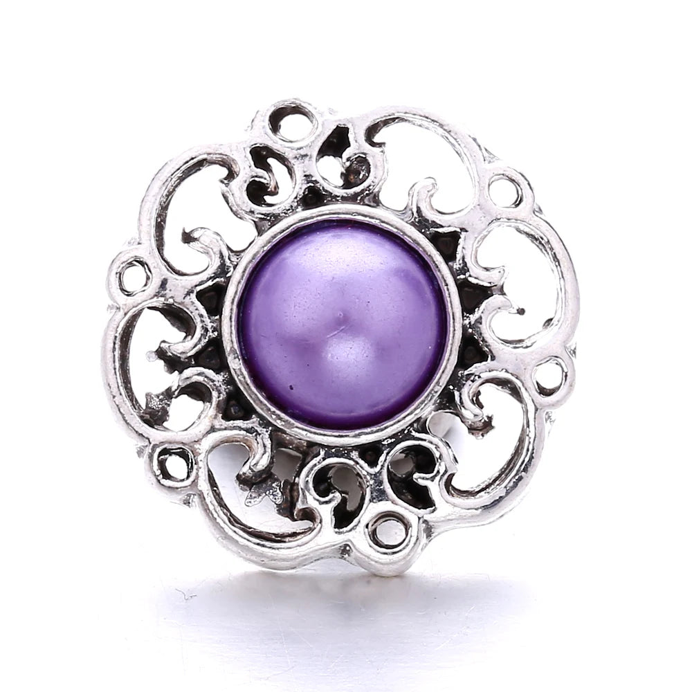 Silver metal snap button with a purple iridescent gemstone center and ornate floral design