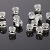 A collection of clear silicone rubber ear back stoppers with copper rings arranged on a dark reflective surface.