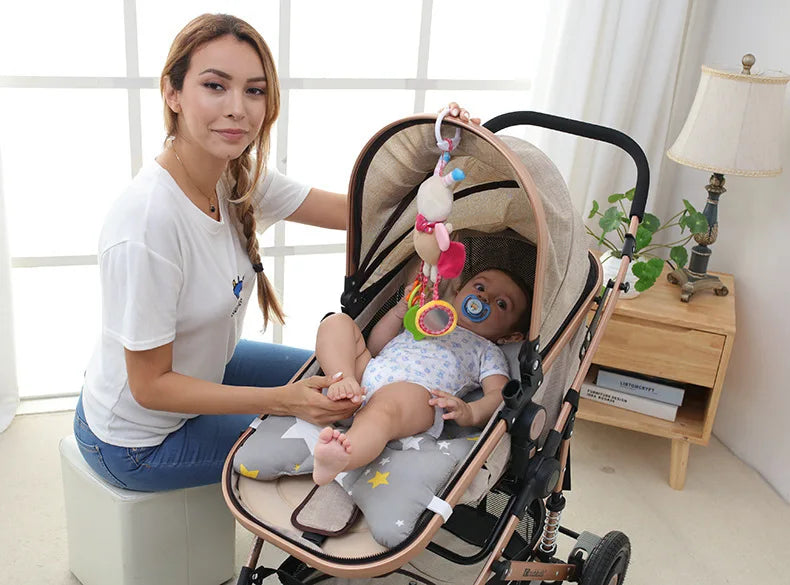 A woman holds a baby in a soft plush stroller mobile with hanging toys and bell.