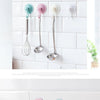 Three silicone kitchen utensils hanging on a white tiled backsplash with suction cup hooks
