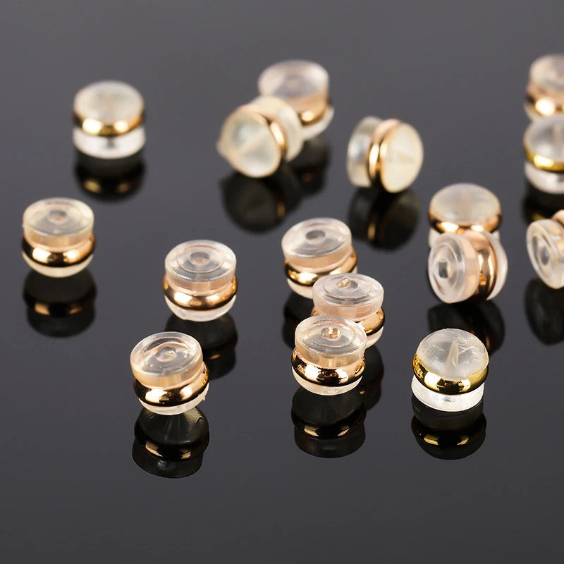 A collection of silicone rubber ear back stoppers with copper rings arranged on a dark reflective surface.