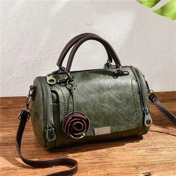 A dark olive green leather crossbody bag with a floral rose pendant resting on a wooden surface.