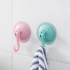 Two suction cup hooks, one pink and one teal, are mounted on a white surface next to a striped towel.
