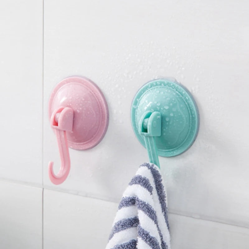 Two suction cup hooks, one pink and one teal, are mounted on a white surface next to a striped towel.