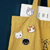 A yellow canvas tote bag featuring embroidered cat patches on the front.