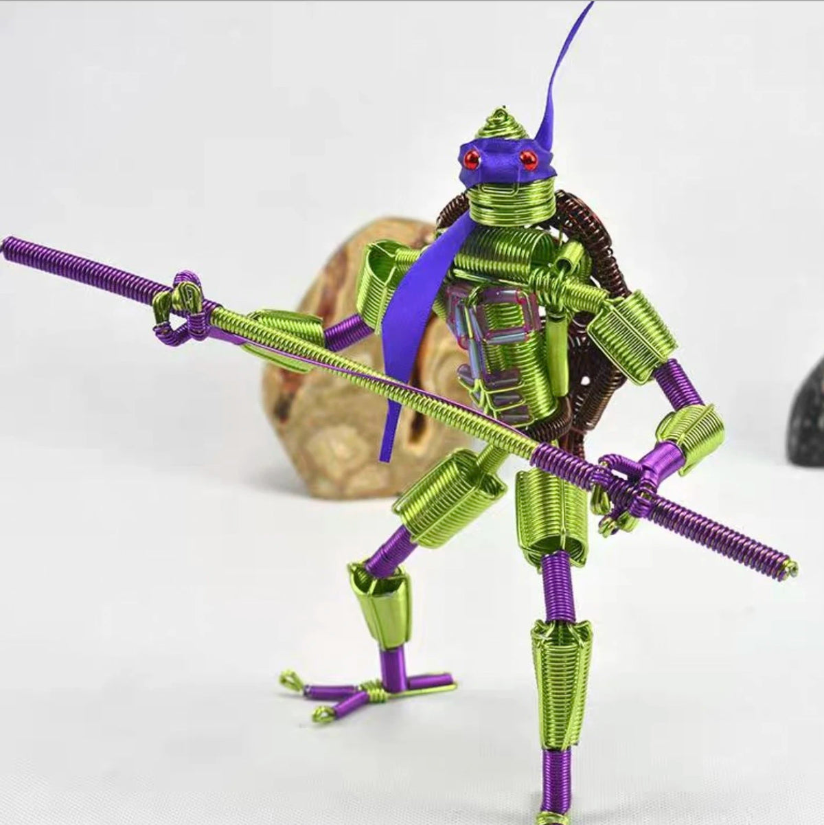 A detailed miniature figure of a stylized insect or creature made from anodized aluminum jewelry wire in purple and green hue
