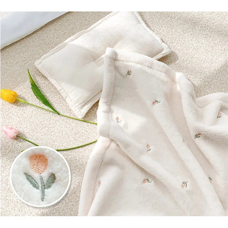 A soft cream coral fleece baby blanket with delicate pink bear embroidery lying on a light textured surface.