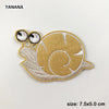 A round, tan embroidered patch of a sea turtle with large eyes and a spiral pattern.