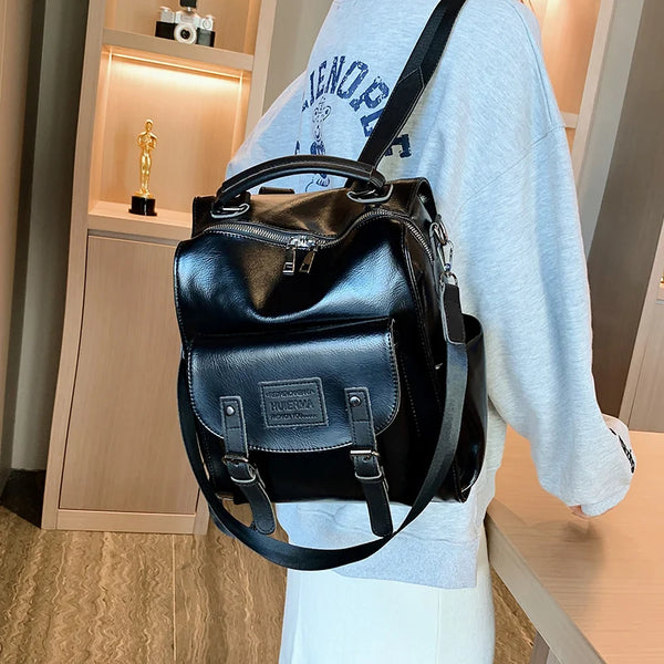 Schwarzer Kunstleder-Rucksack aus modischer Kleidung, getragen von einer Person, in einem hellen Raum präsentiert.