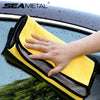 A hand is wiping a dark car surface with a yellow microfiber car care towel.