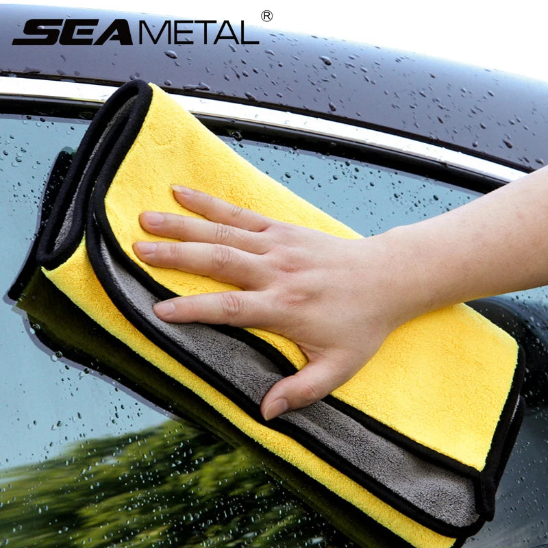 A hand is wiping a dark car surface with a yellow microfiber car care towel.