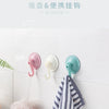 Three silicone suction cup hooks in pink, white, and teal hanging on a white surface.