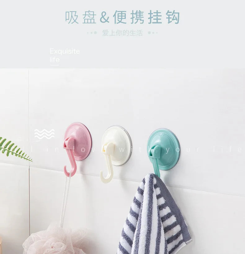 Three silicone suction cup hooks in pink, white, and teal hanging on a white surface.
