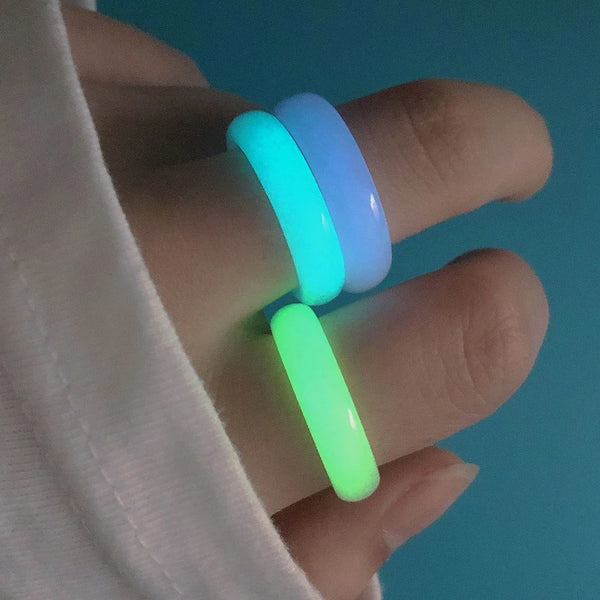 Una mano sostiene tres anillos de pareja de piedra luminosos en tonos cian, azul y verde contra un fondo azul.