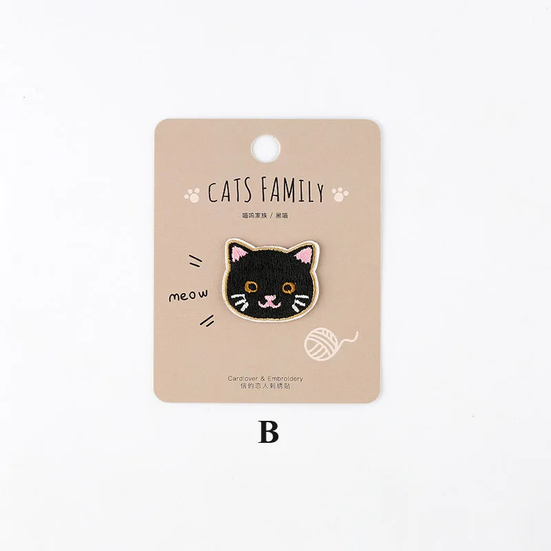 A beige iron-on patch featuring an embroidered black cat face with orange eyes and whiskers.