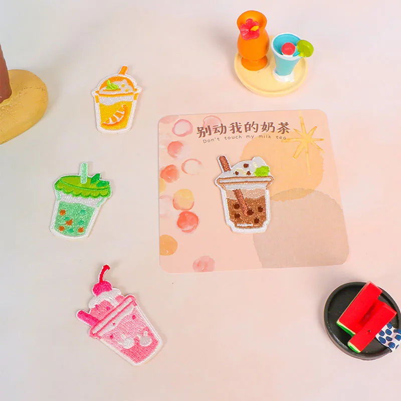 A collection of food-themed embroidered iron-on patches featuring various desserts and drinks on a light pink background.