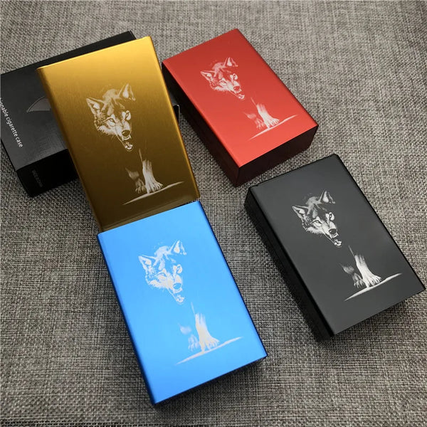 Three laser-engraved aluminum cigarette cases in gold, red, and blue featuring a wolf design on a gray fabric surface.