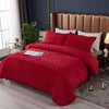 A vibrant red quilted velvet bedspread with a textured pattern is displayed on a bed in a modern bedroom setting.