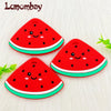 A bright red watermelon silicone teether pendant with a cute face design resting on a white surface.