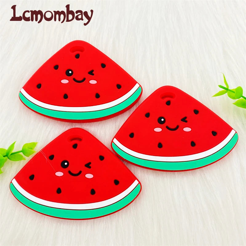 A bright red watermelon silicone teether pendant with a cute face design resting on a white surface.