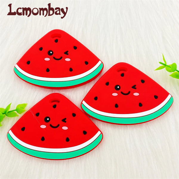 A bright red watermelon silicone teether pendant with a cute face design resting on a white surface.