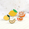 A set of enamel fruit brooches featuring lemons, oranges, and a citrus slice on a white background.