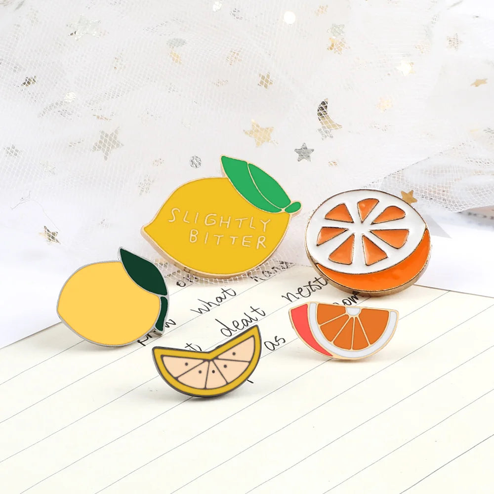 A set of enamel fruit brooches featuring lemons, oranges, and a citrus slice on a white background.