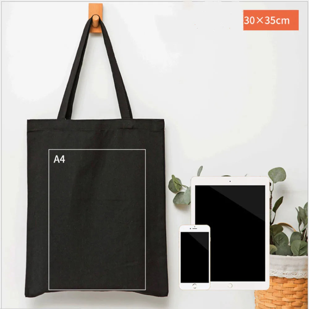 A black canvas tote bag with an A4 sized square printed on it, displayed next to a tablet and smartphone.