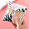 A hand holds a pink floral cosmetic storage pouch with a natural fiber closure on a pink background.