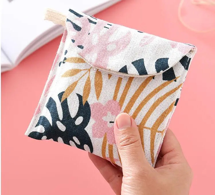 A hand holds a pink floral cosmetic storage pouch with a natural fiber closure on a pink background.